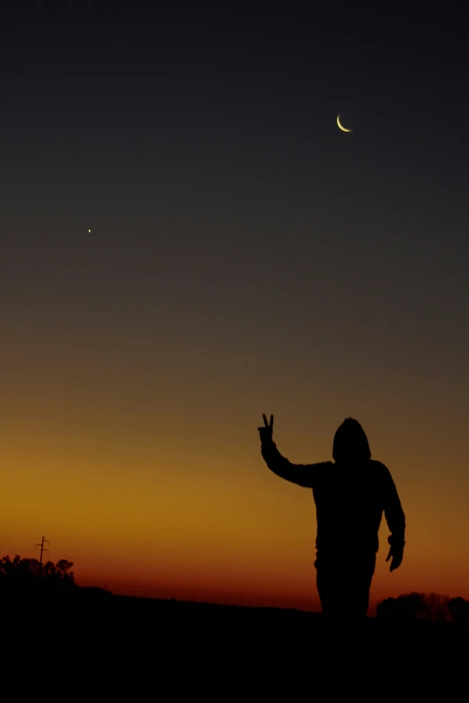 a man with a finger up is standing in the sunset