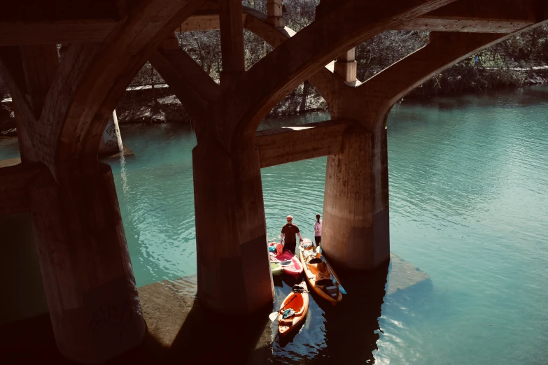 several people in small boats moving under a bridge