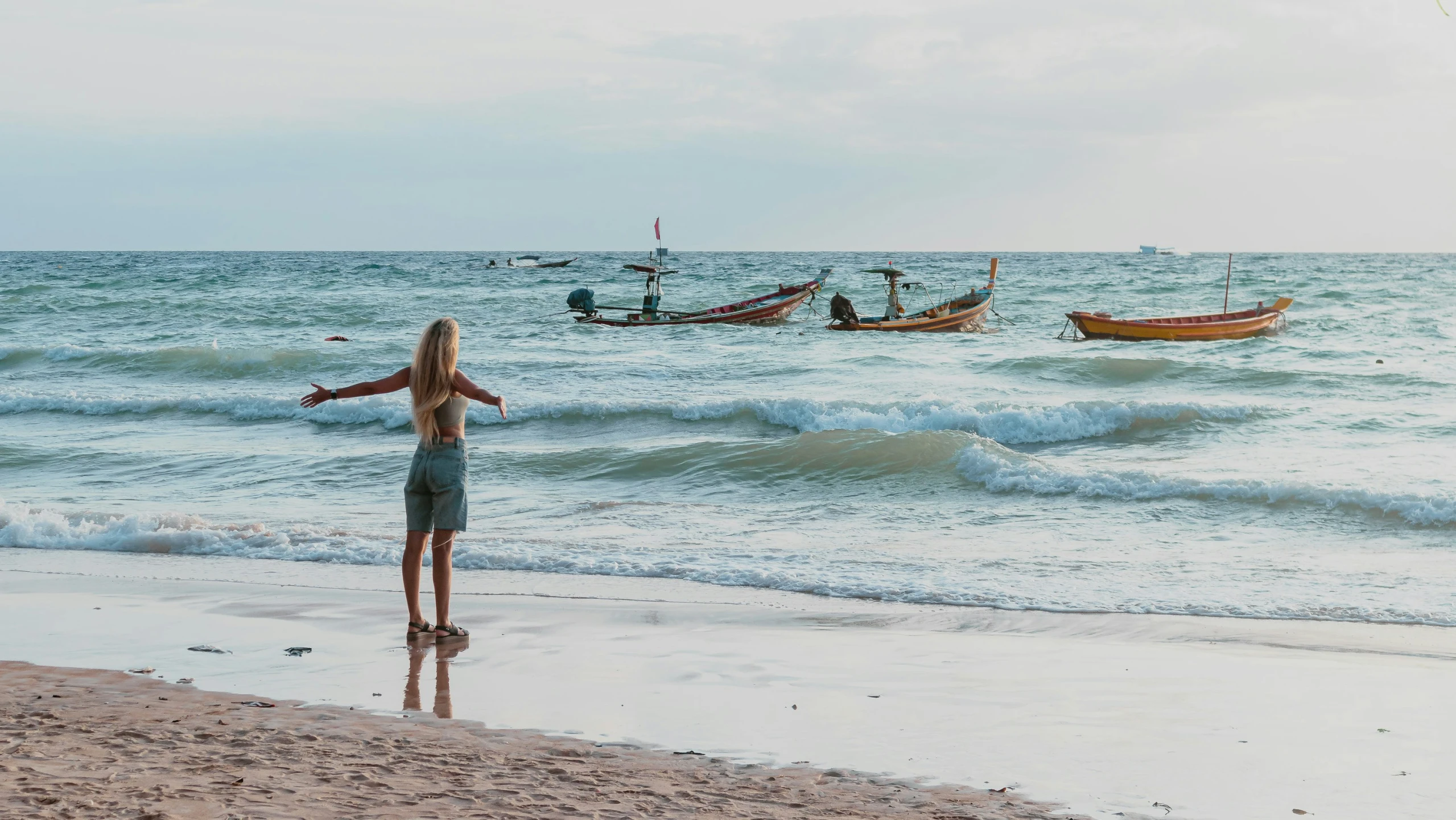 there are boats in the distance as a woman on a beach stands by the water