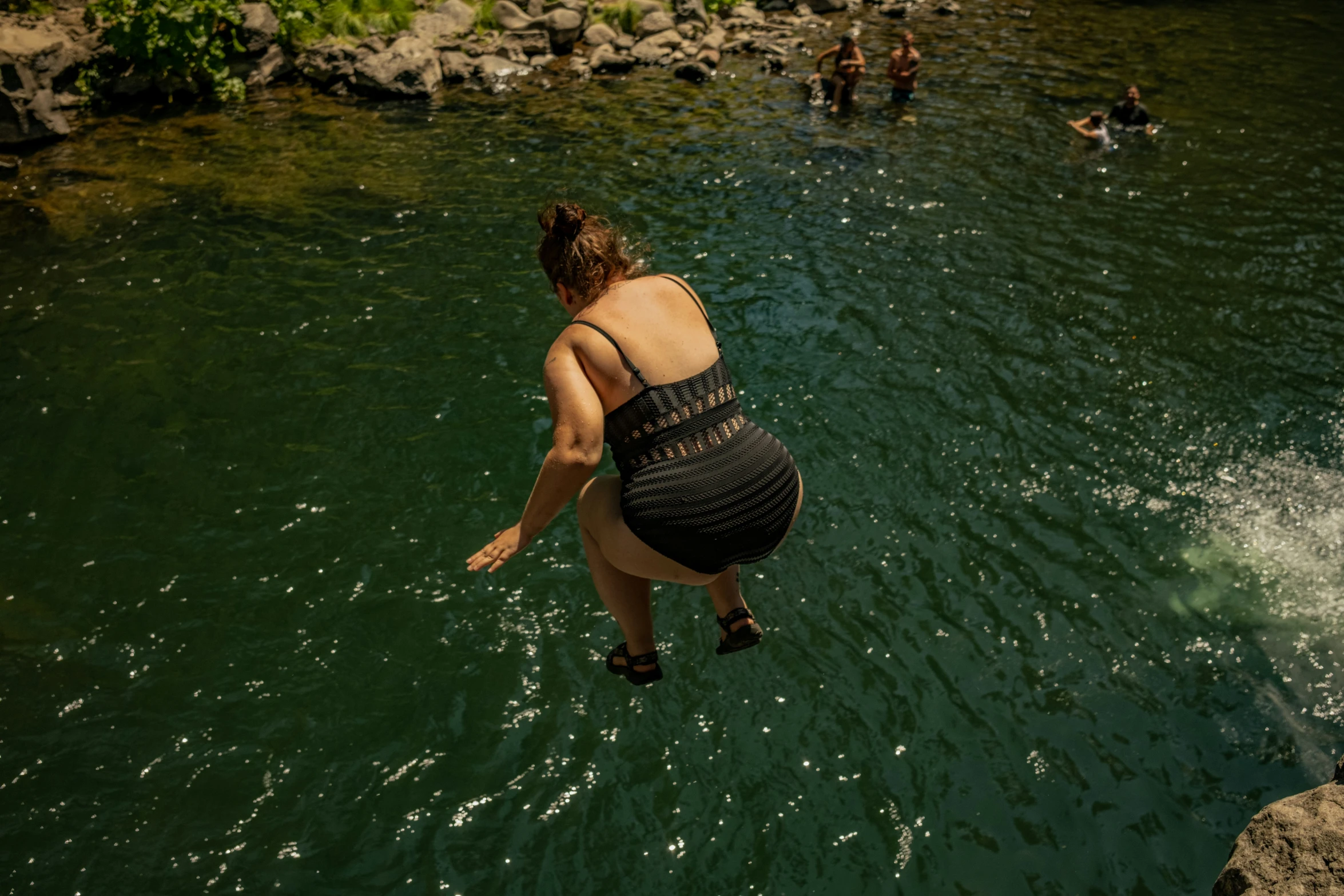 a woman jumping into a lake with others swimming nearby