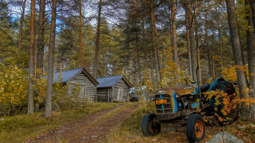 an old tractor sitting on the side of a trail in a forest