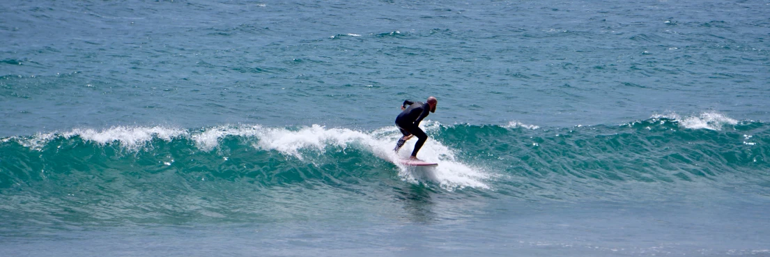 a man in black wet suit riding a wave on a white surfboard