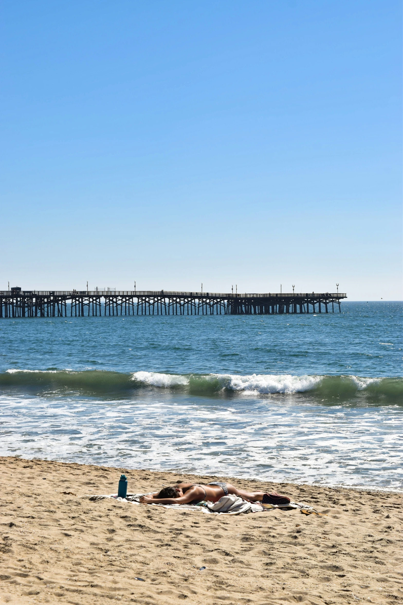 person laying on sandy beach next to pier with ocean in background