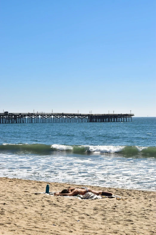 person laying on sandy beach next to pier with ocean in background