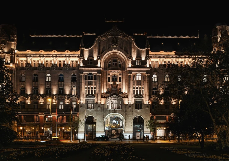 a lit building stands behind trees and other buildings