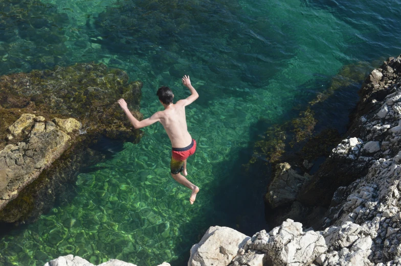a man in swimming trunks jumping off rocks into the ocean