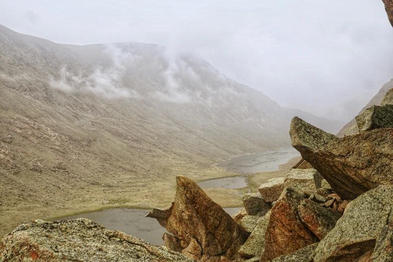 an image of rocks and water that have clouds rolling over the mountains