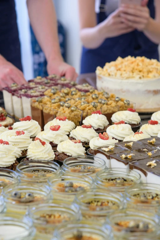 two people standing at a table with plates of cake and pastries