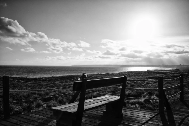 a wooden bench near the ocean under a bright sun