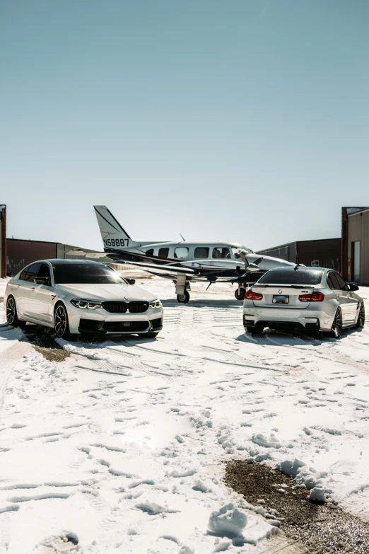 two luxury cars next to an airplane on snow covered ground