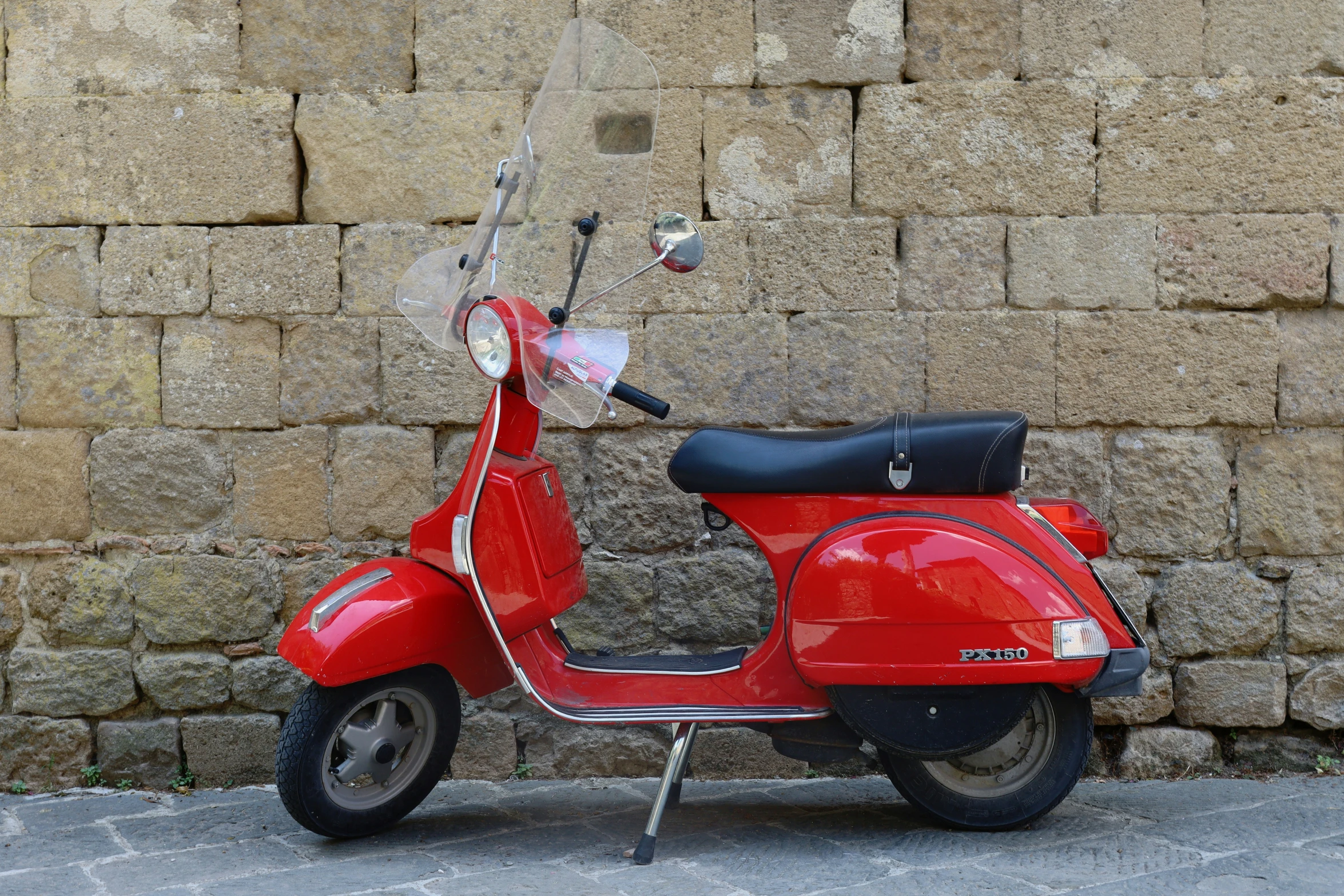 red moped with two rear lights sitting by a wall