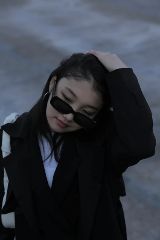 a young asian woman in a dark suit covers her face with her glasses