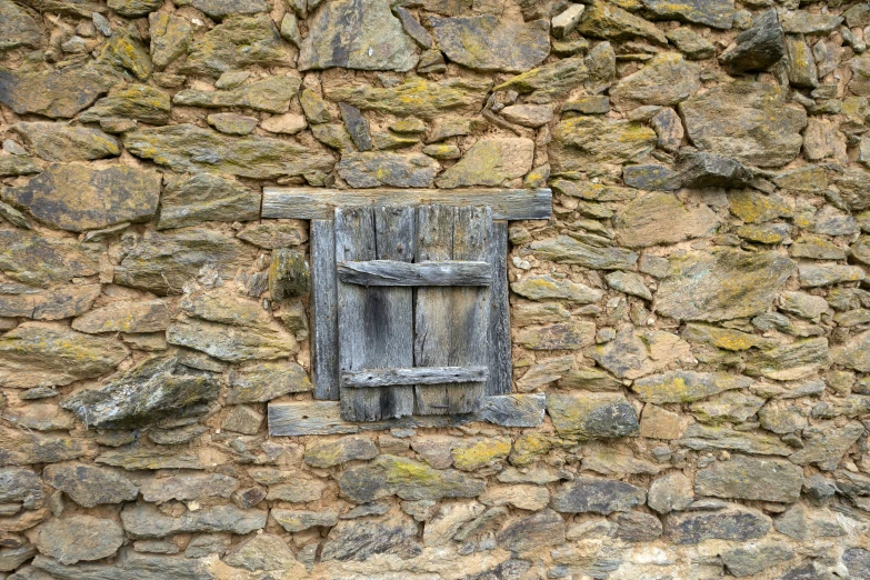 a weathered window that is next to a stone wall