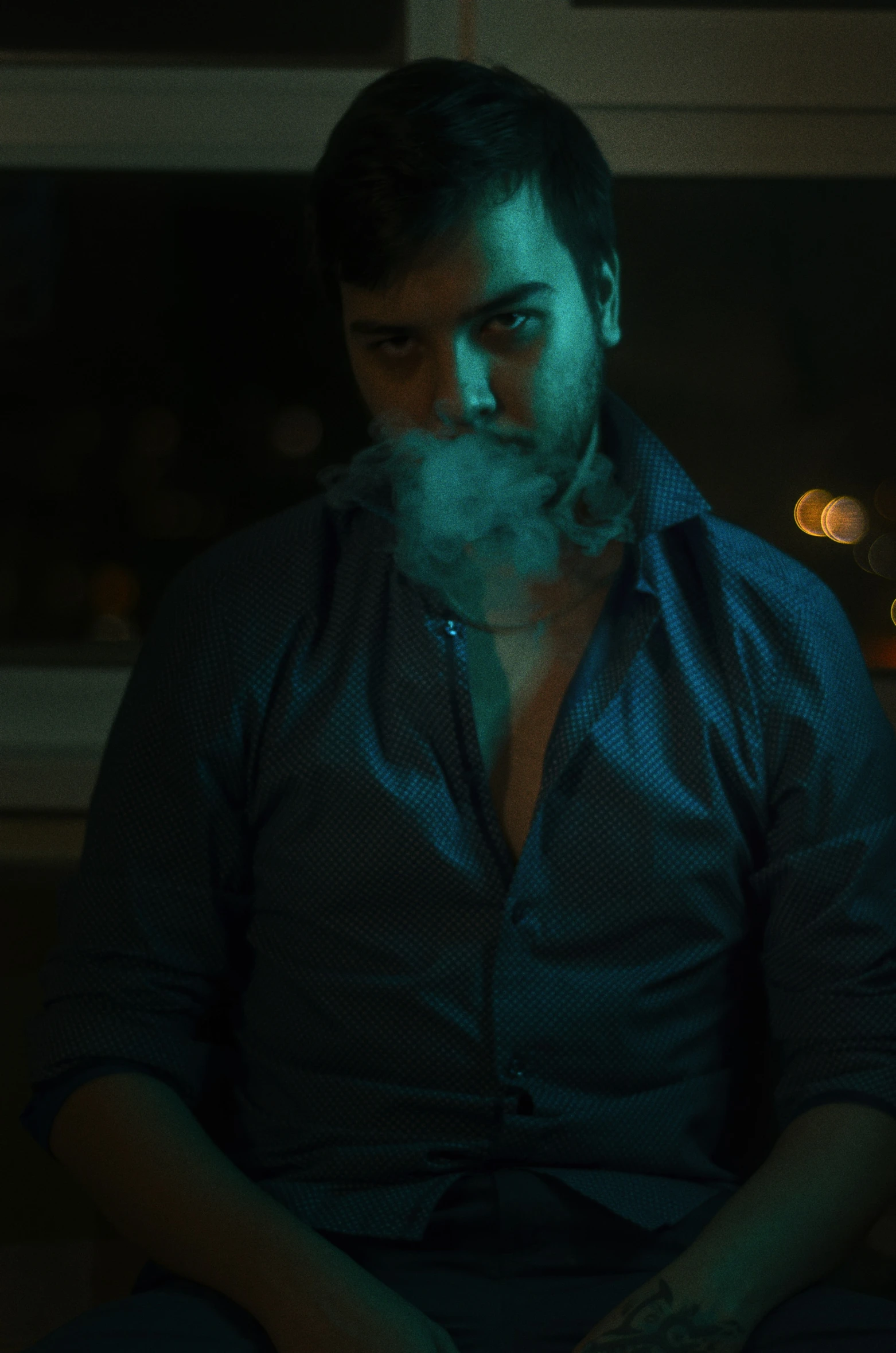 a man sits in a dark room with a smokey cigarette coming out of his mouth