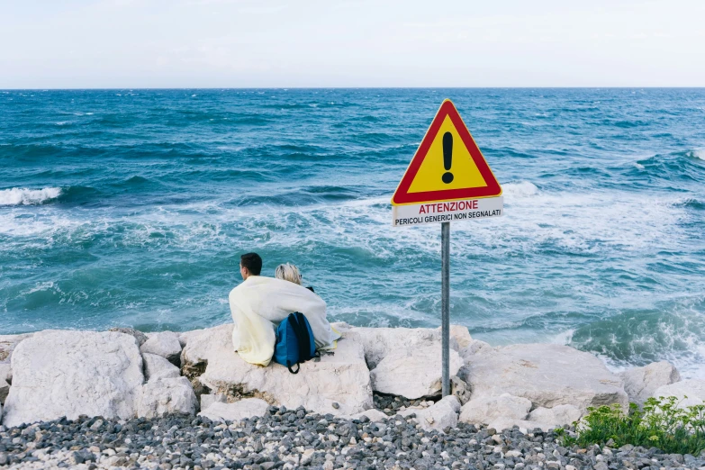 a man sits on the rocks near a sign reading attention