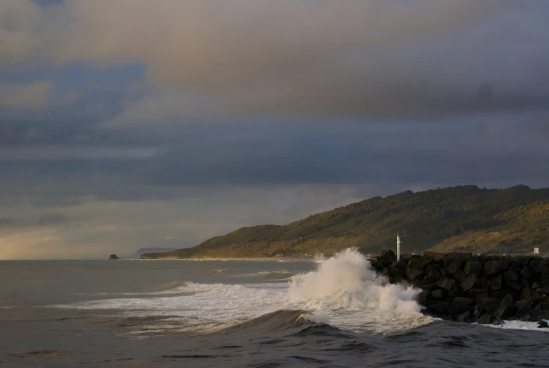 waves crash into the rocky shore as a light house stands on a cliff