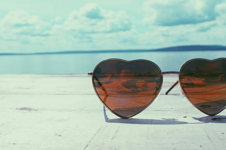 sunglasses with reflection of two people and one another on the edge of a boardwalk near the ocean