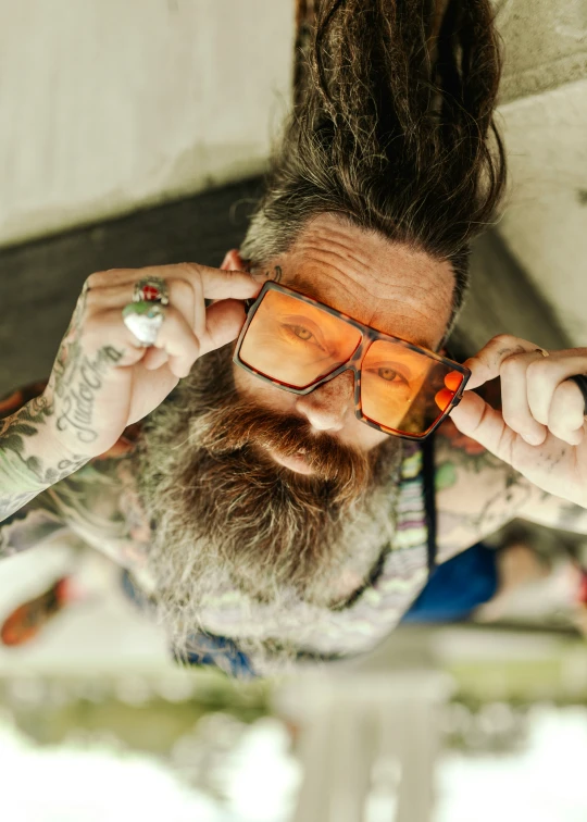 a man with a long beard and glasses looks at his reflection in the mirror