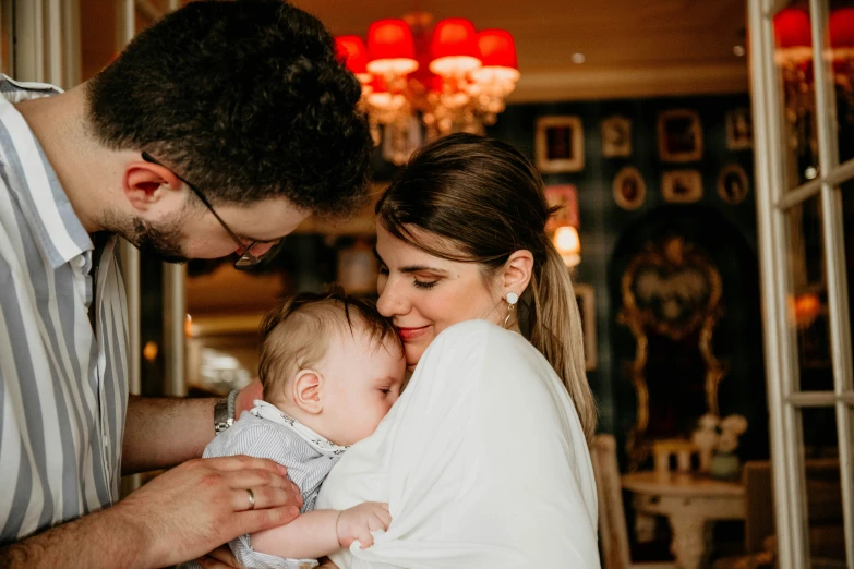 a woman and man hold their baby while the baby's face is partially covered