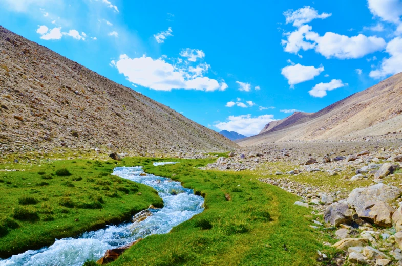 a river in between some hills, next to a green field