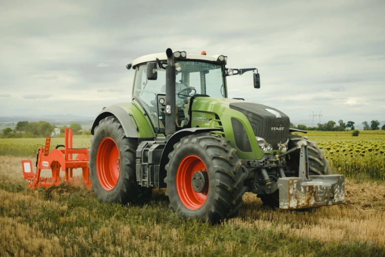 a green and red tractor with bright orange wheels sits in a field