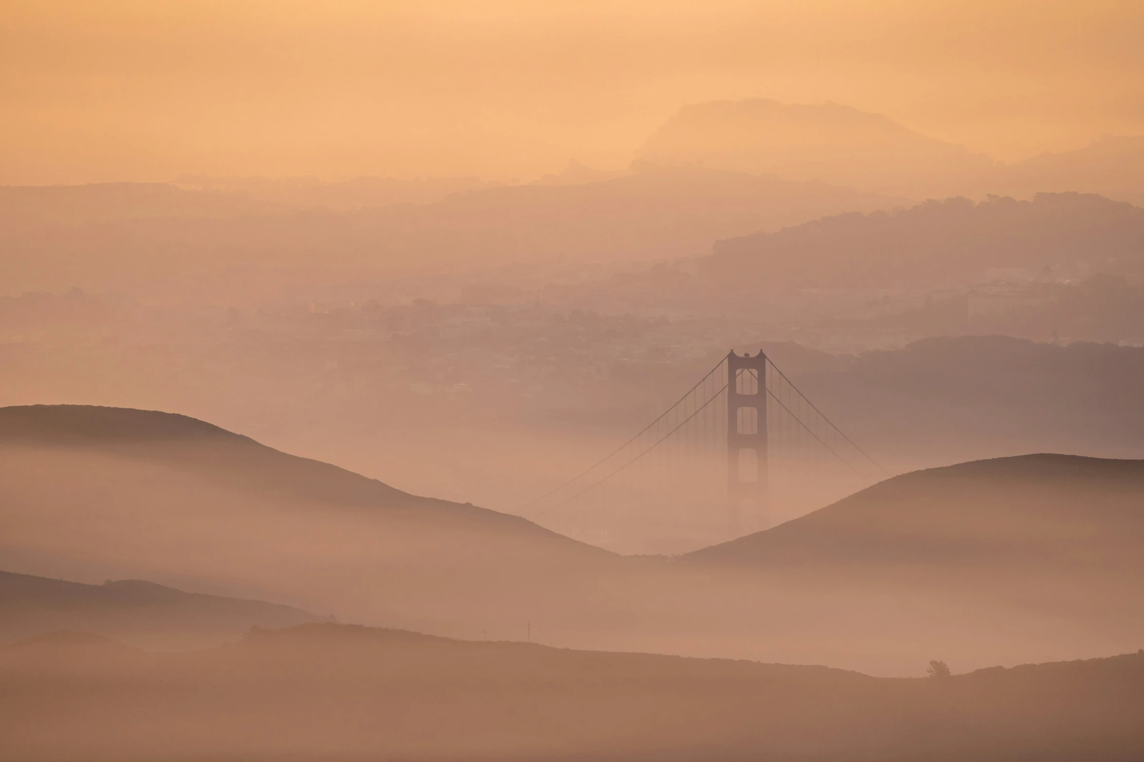 fog hangs over hills and mountains, and a light tower is visible