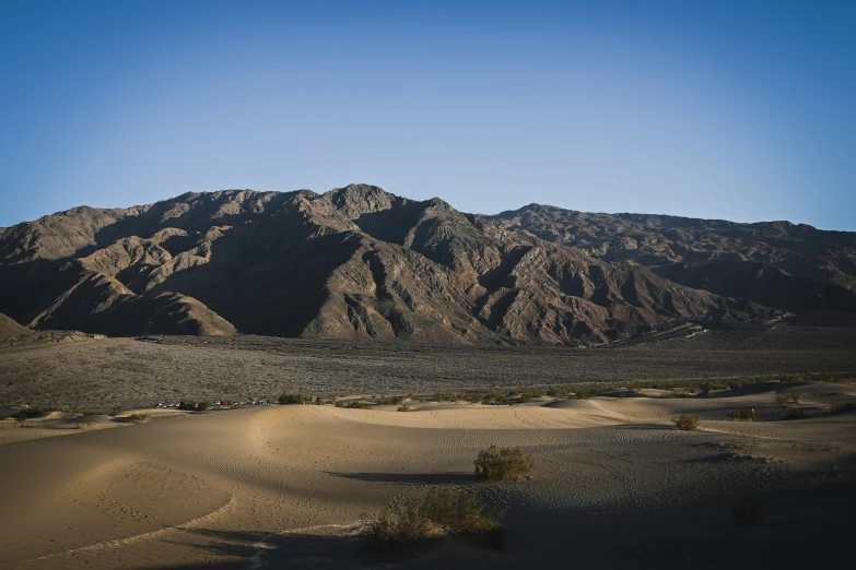 a very large mountain in the distance with sand and bushes