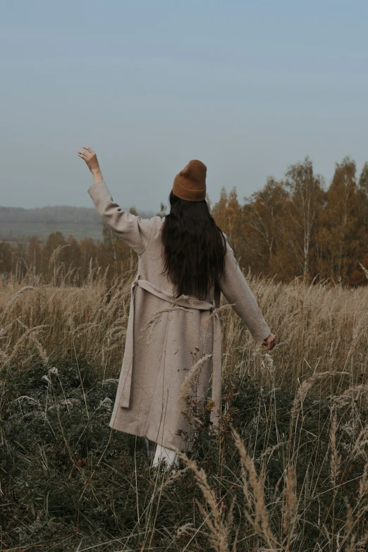 a girl standing in tall grass holding her arms up in the air