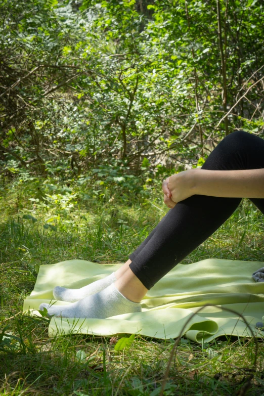 the person with black shoes is sitting on a yellow blanket in a forest