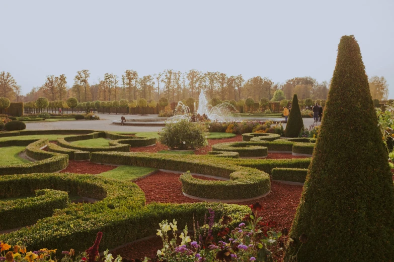 people are walking along a formal garden in a park