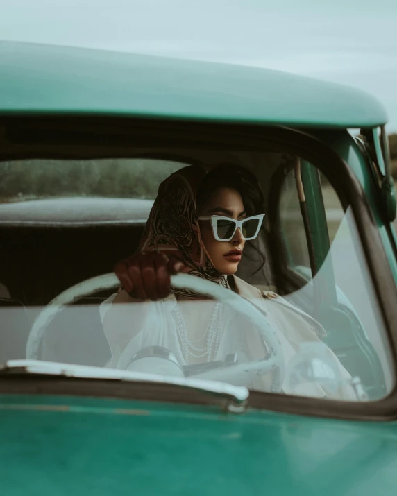 a woman driving a green car with a scarf on