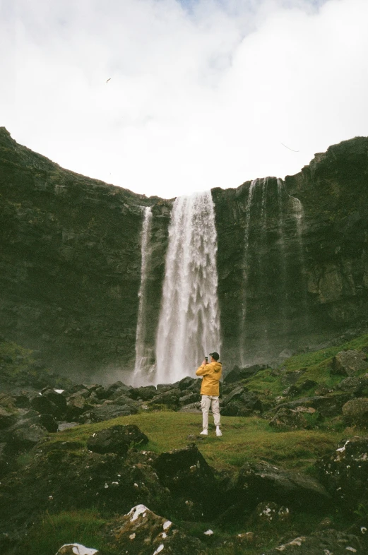 man taking po of water fall on a cloudy day