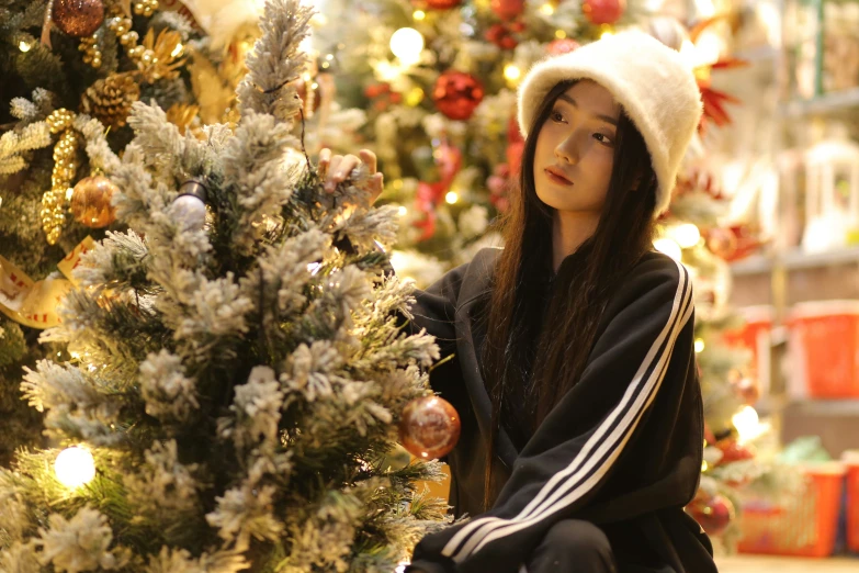 a child wearing a hat is sitting by the christmas tree
