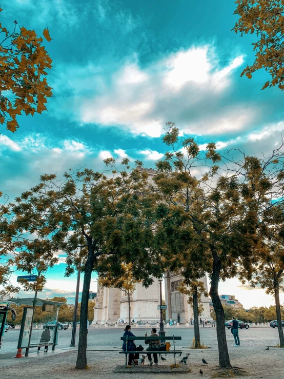 two people are sitting at a bench under trees