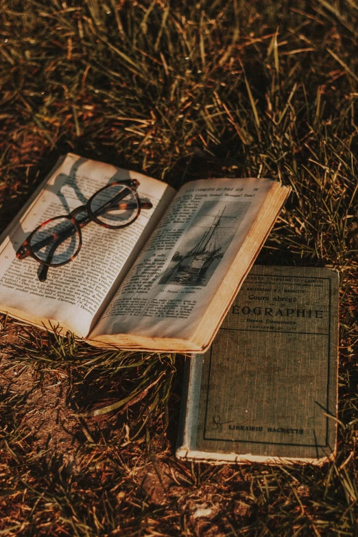 an open book laying on top of a field with glasses