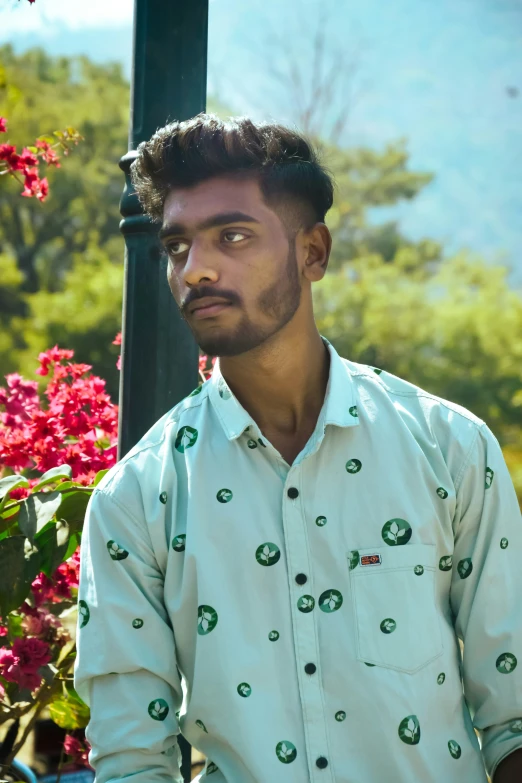 a man in blue and green shirt sitting by some flowers