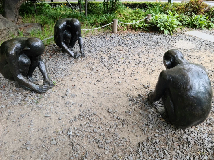 two silver statues on gravel, one holding the head of another sitting