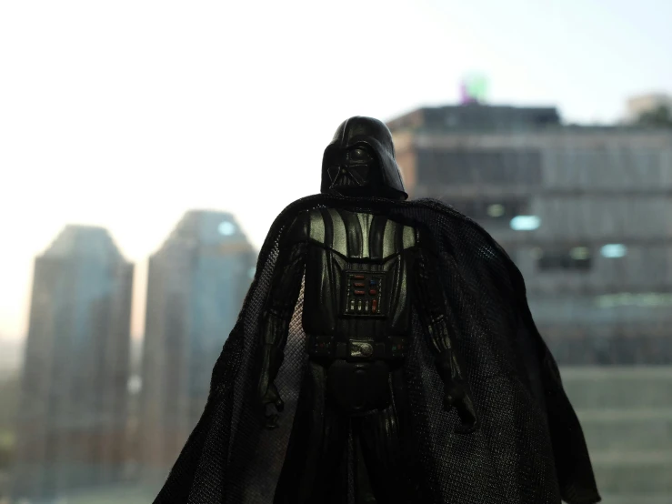 a toy darth vader with city buildings in the background