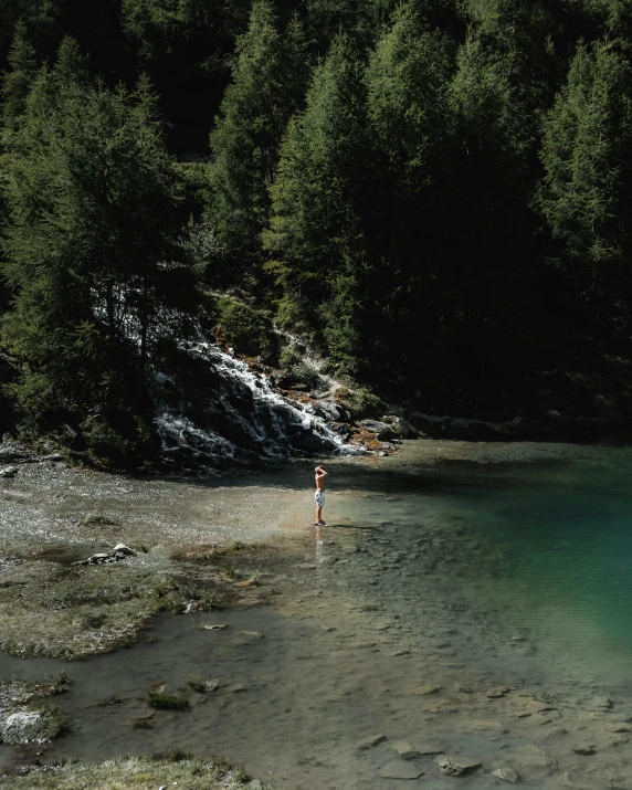 a man is wading in shallow water by the side of a waterfall