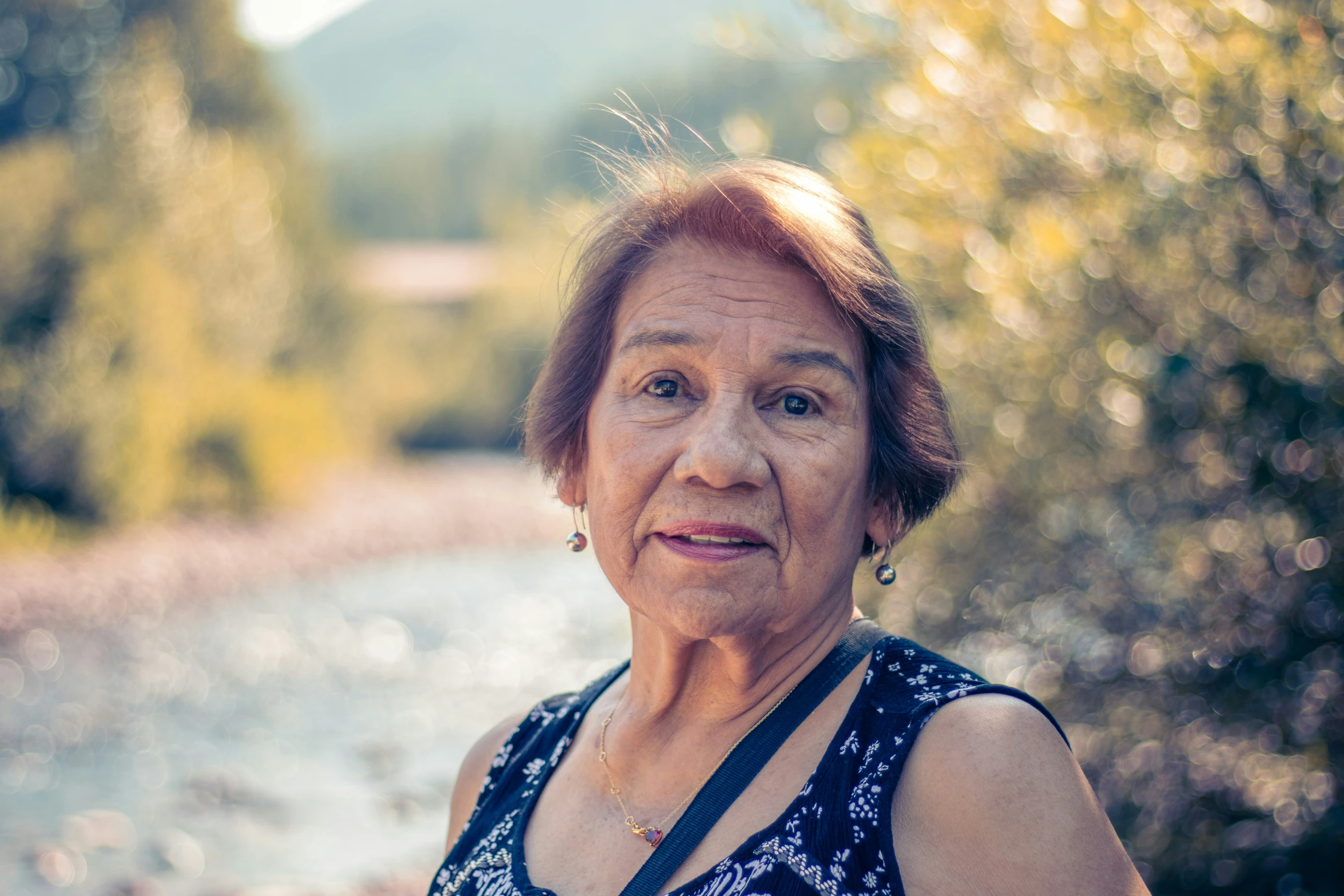 an elderly woman with glasses standing in front of a river