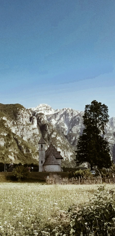 a stone church stands in a field surrounded by mountains