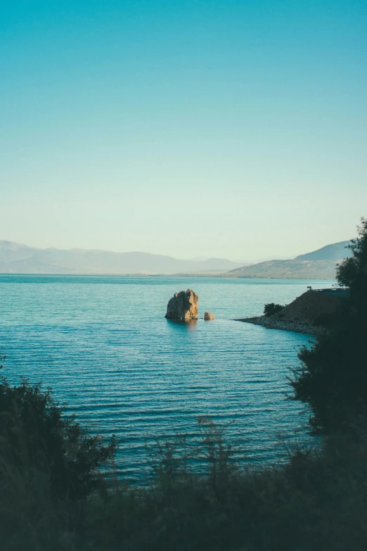 some small rock in a body of water with a mountain range behind it