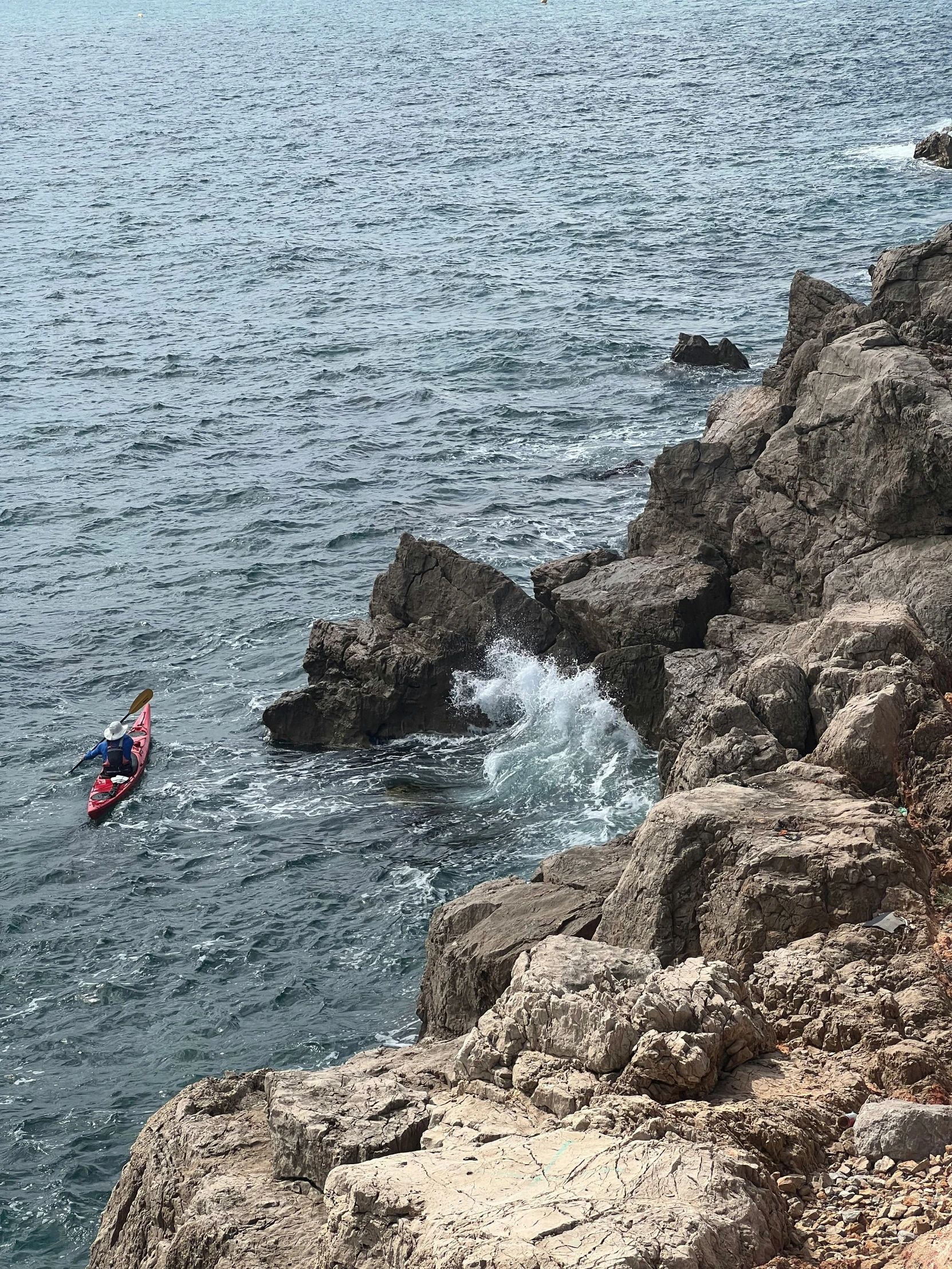 person on kayak sailing along rocky coastline with open ocean