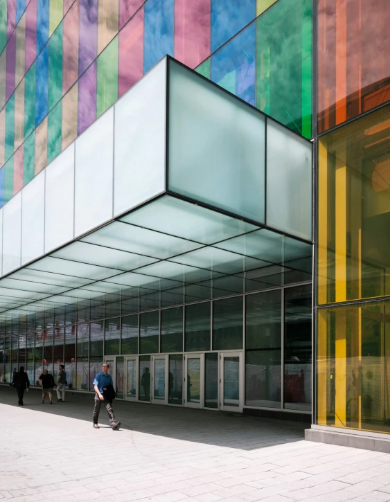 a man is walking along with his skateboard in front of a building with multicolored glass panels