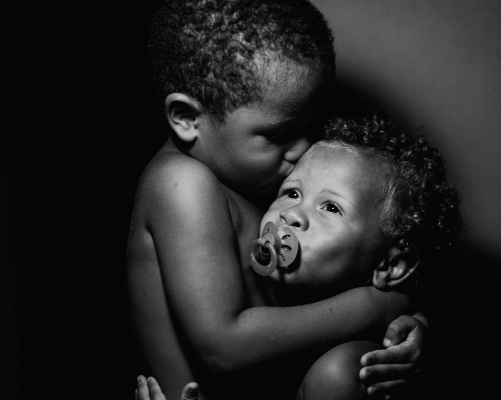 two young children hugging one another on a dark background