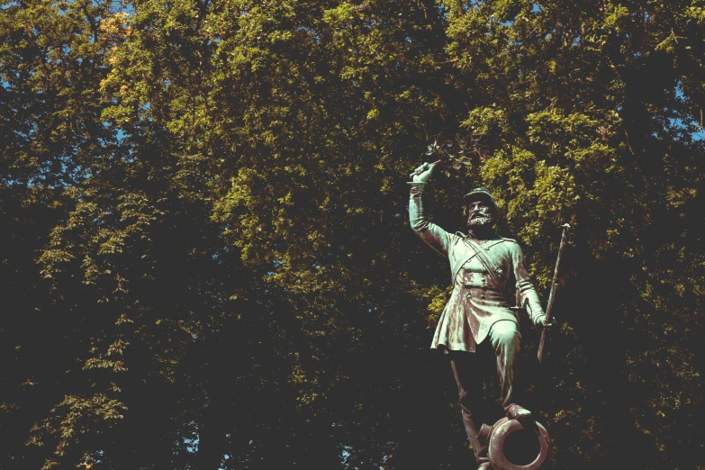 statue of indian warrior holding up a nch in front of tree tops
