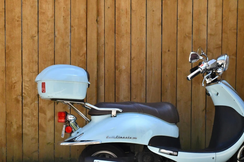 a moped sits against a wooden wall by itself