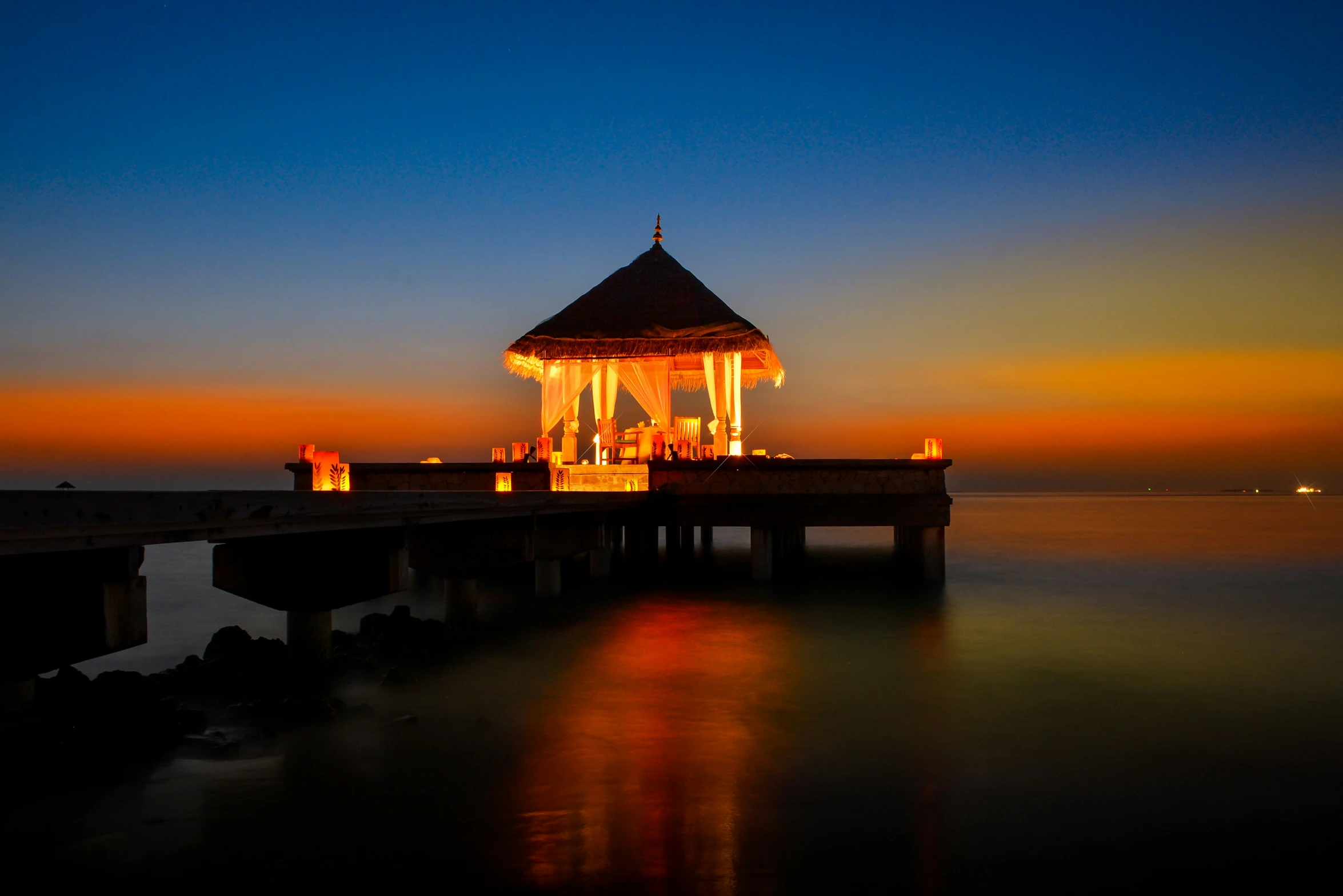 a gazebo with people sitting at the end during sunset