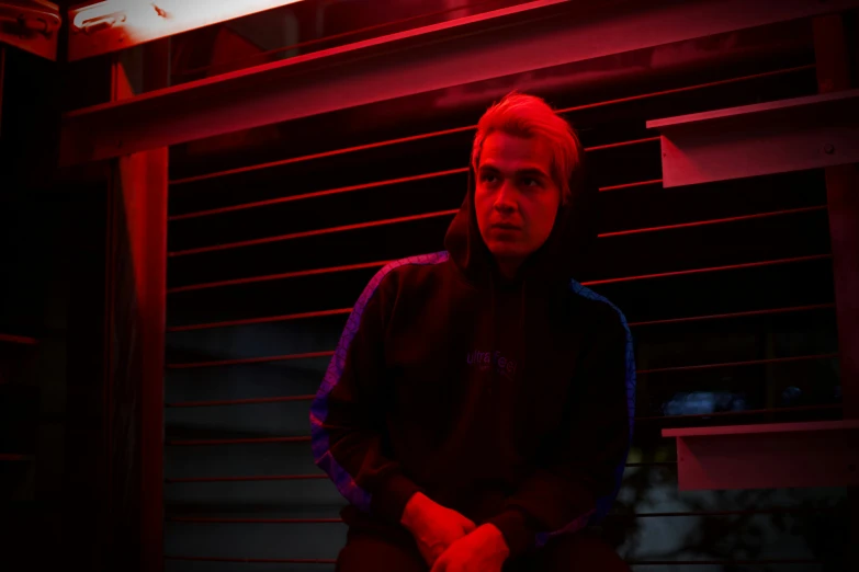 man sitting in dark room with red light on blinds