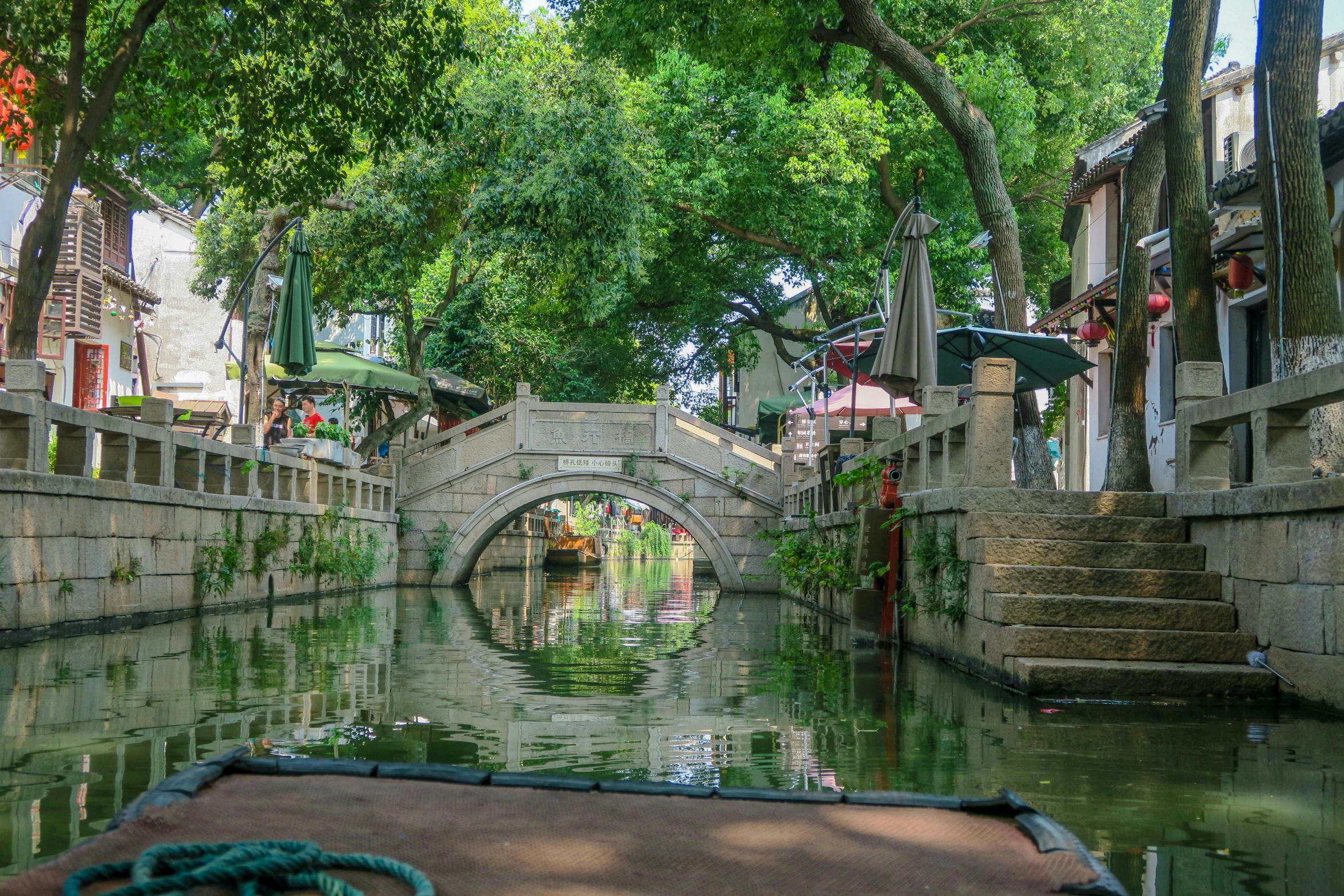 a boat is going down a narrow canal with a bridge and lots of trees